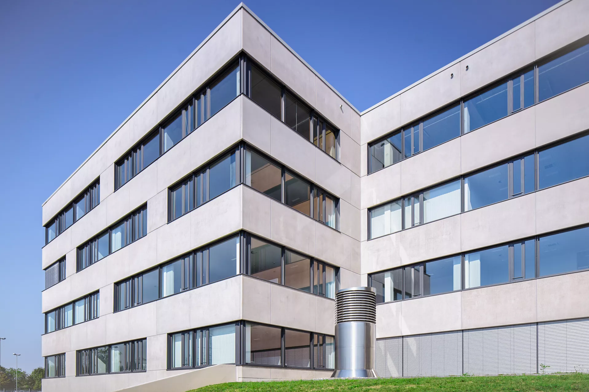 Modernes 4-stöckiges Bürogebäude mit einer Fassade aus Betonplatten und großflächigen Fenstern. Die Kamer blickt vom Boden herauf.