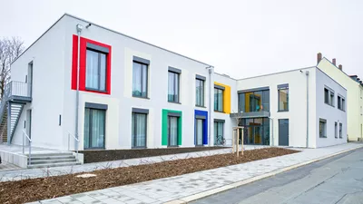 Modernes 2-stöckiges Gebäude mit bodentiefen Fenstern und Farbakzenten um manche Fenster (rot, grün, blau, gelb)