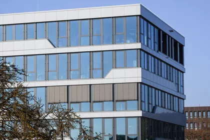 Blick auf ein großes 5-stöckiges bürogebäude, das sehr viele Fenster hat und sehr modern aussieht. Vor dem gebäude ist eine Wiese mit einem Baum. 