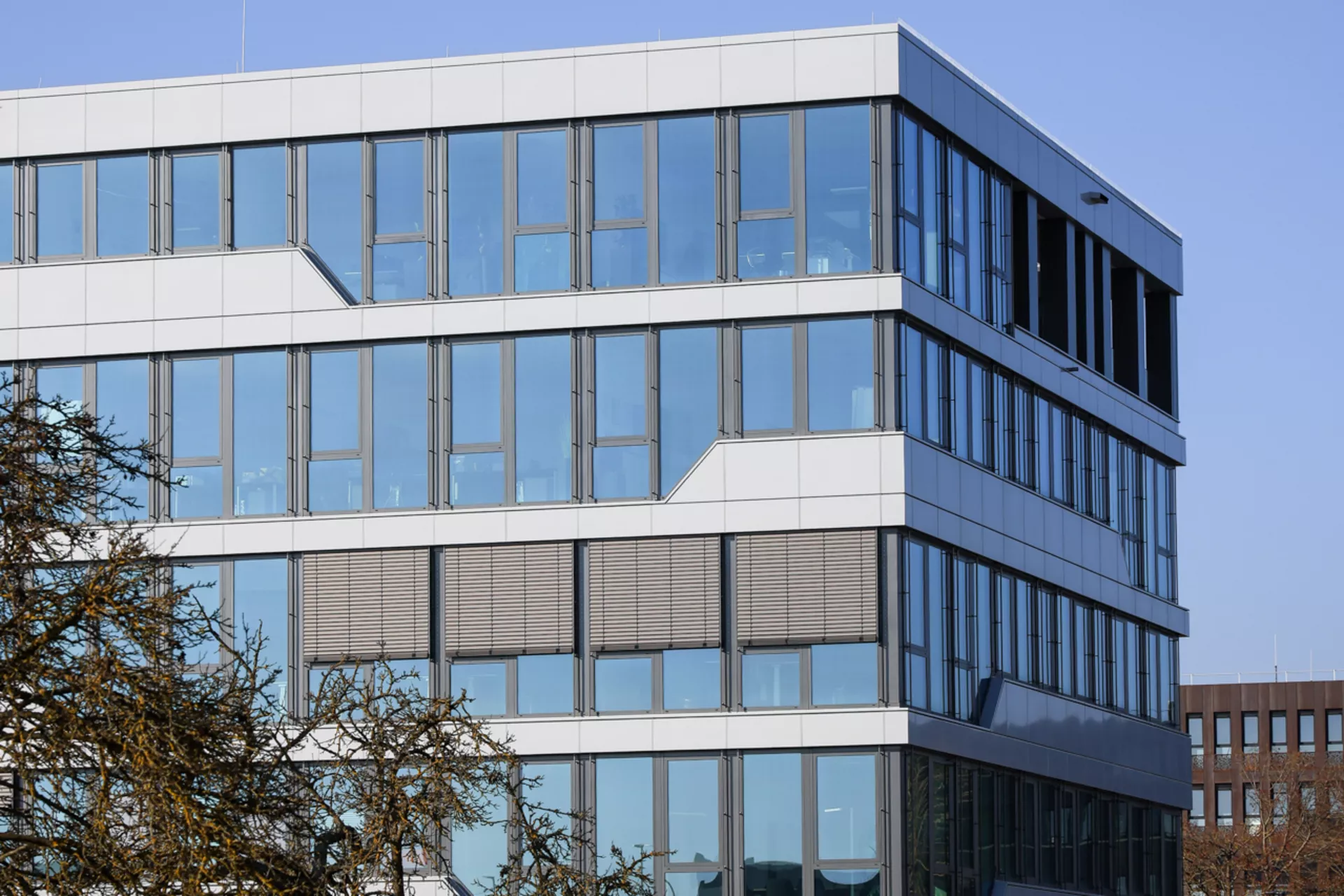 Blick auf ein großes 5-stöckiges bürogebäude, das sehr viele Fenster hat und sehr modern aussieht. Vor dem gebäude ist eine Wiese mit einem Baum. 