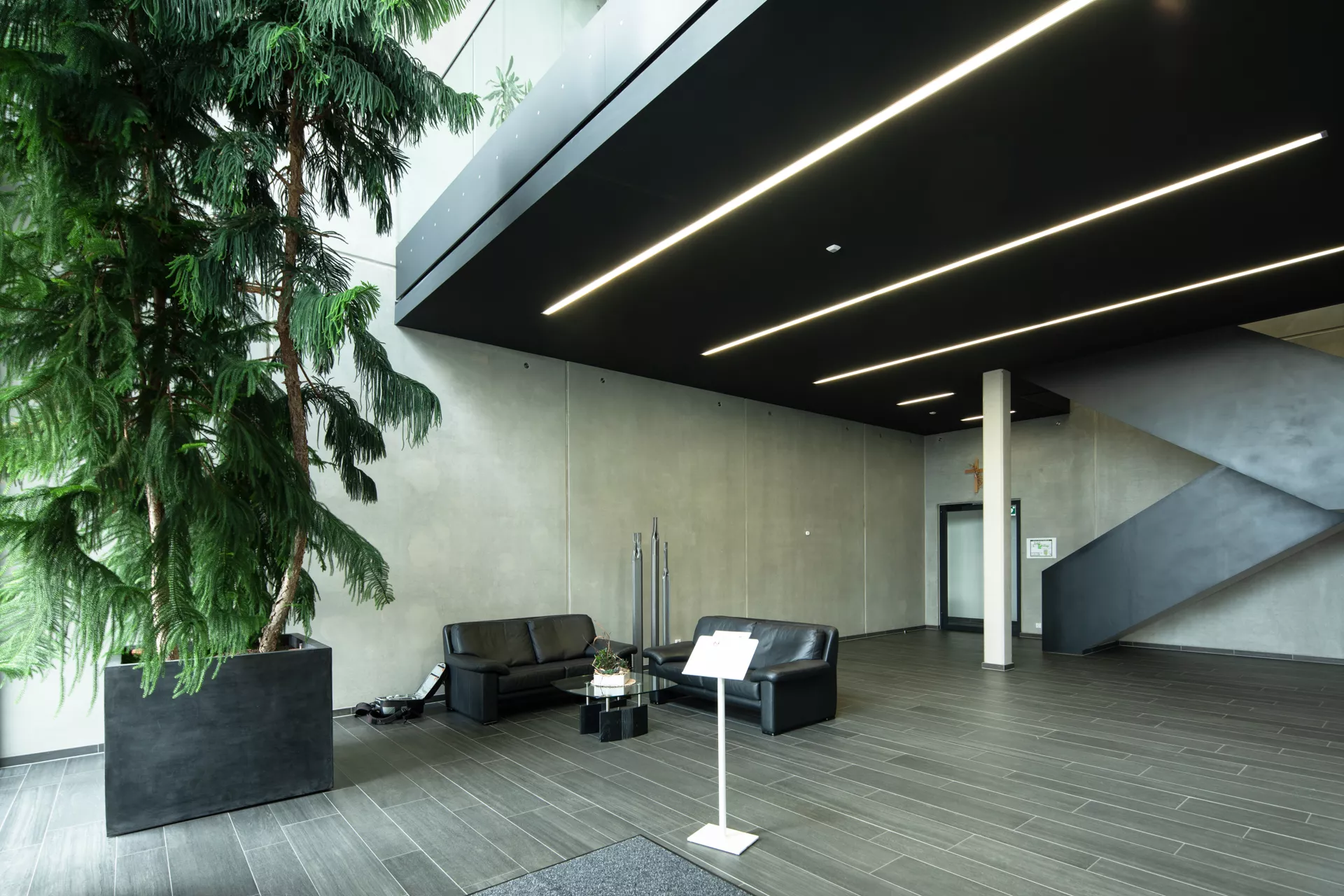 Innenansicht des Gebäudeeingangs. Links ist ein großer Baum und daneben zwei ofas und ein Tisch. Rechts ist die Treppe, die in den zweiten Stock führt.