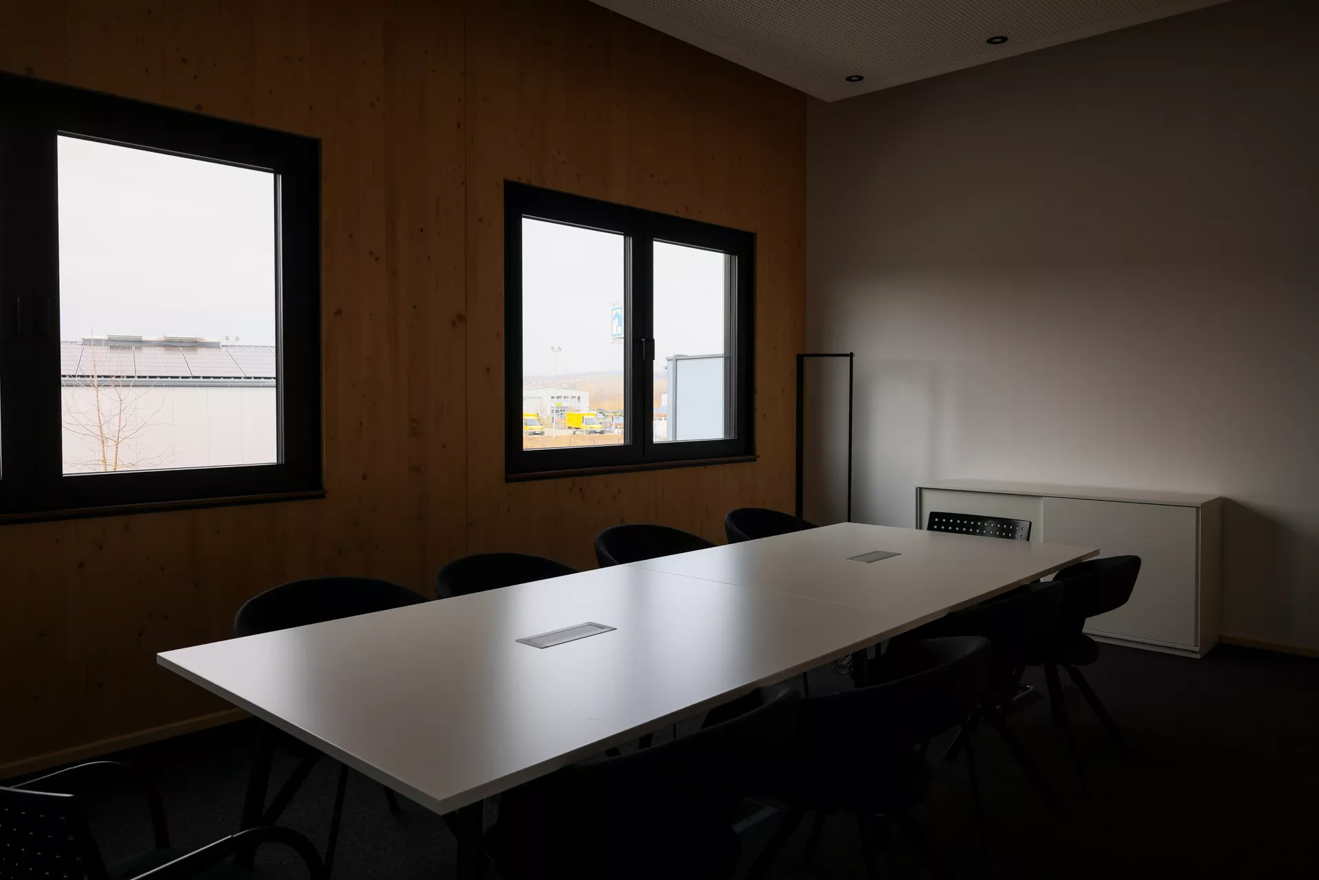 Besprechungsraum mit einem großen Tisch und Stühlen mit zwei großen Fenstern in der Wand im Hintergrund.