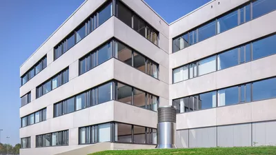 Modernes 4-stöckiges Bürogebäude mit einer Fassade aus Betonplatten und großflächigen Fenstern. Die Kamer blickt vom Boden herauf.