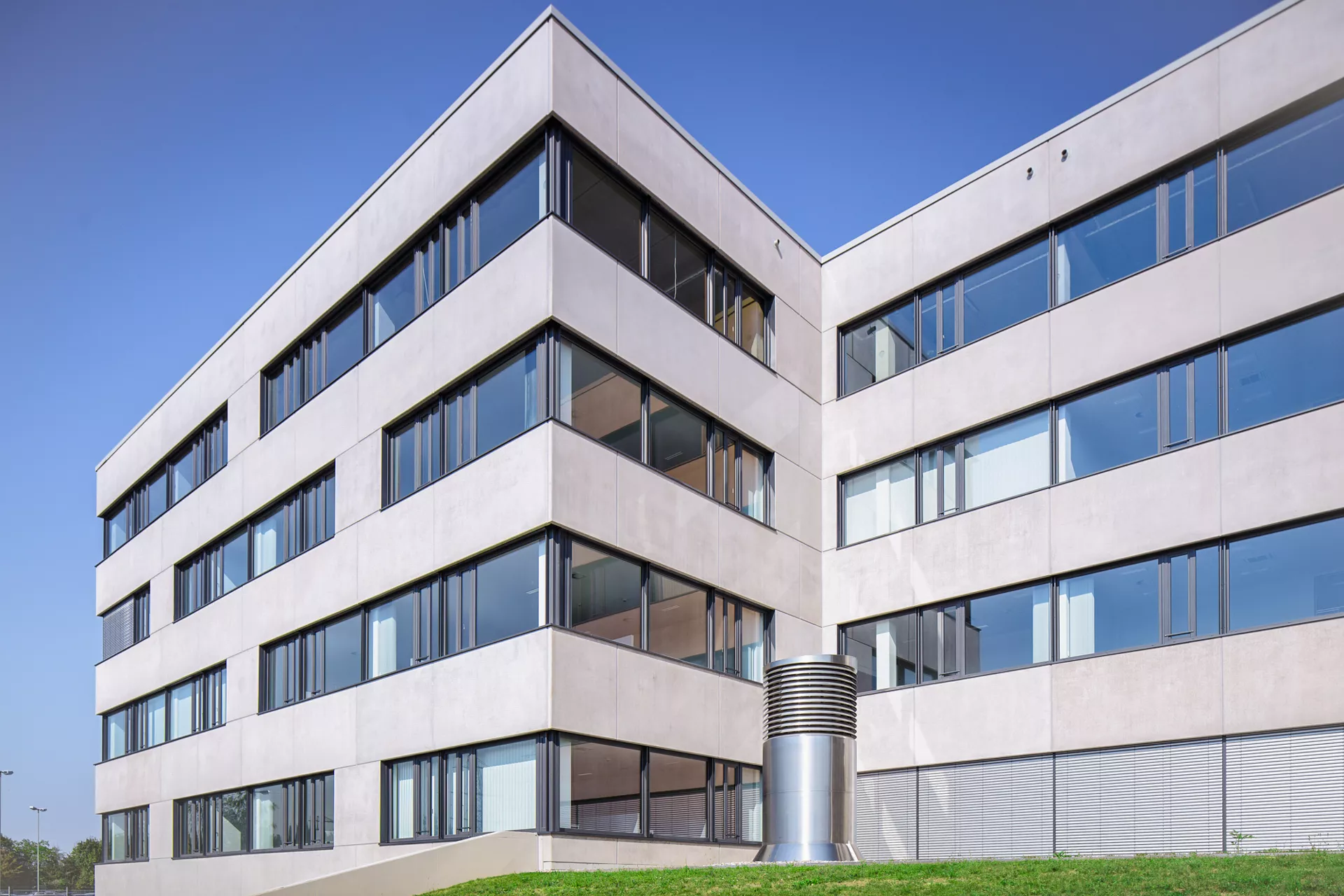 Modernes 4-stöckiges Bürogebäude mit einer Fassade aus Betonplatten und großflächigen Fenstern. Die Kamer blickt vom Boden herauf.