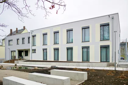 2-stöckiges weißes Gebäude mit bodentiefen Fenstern.