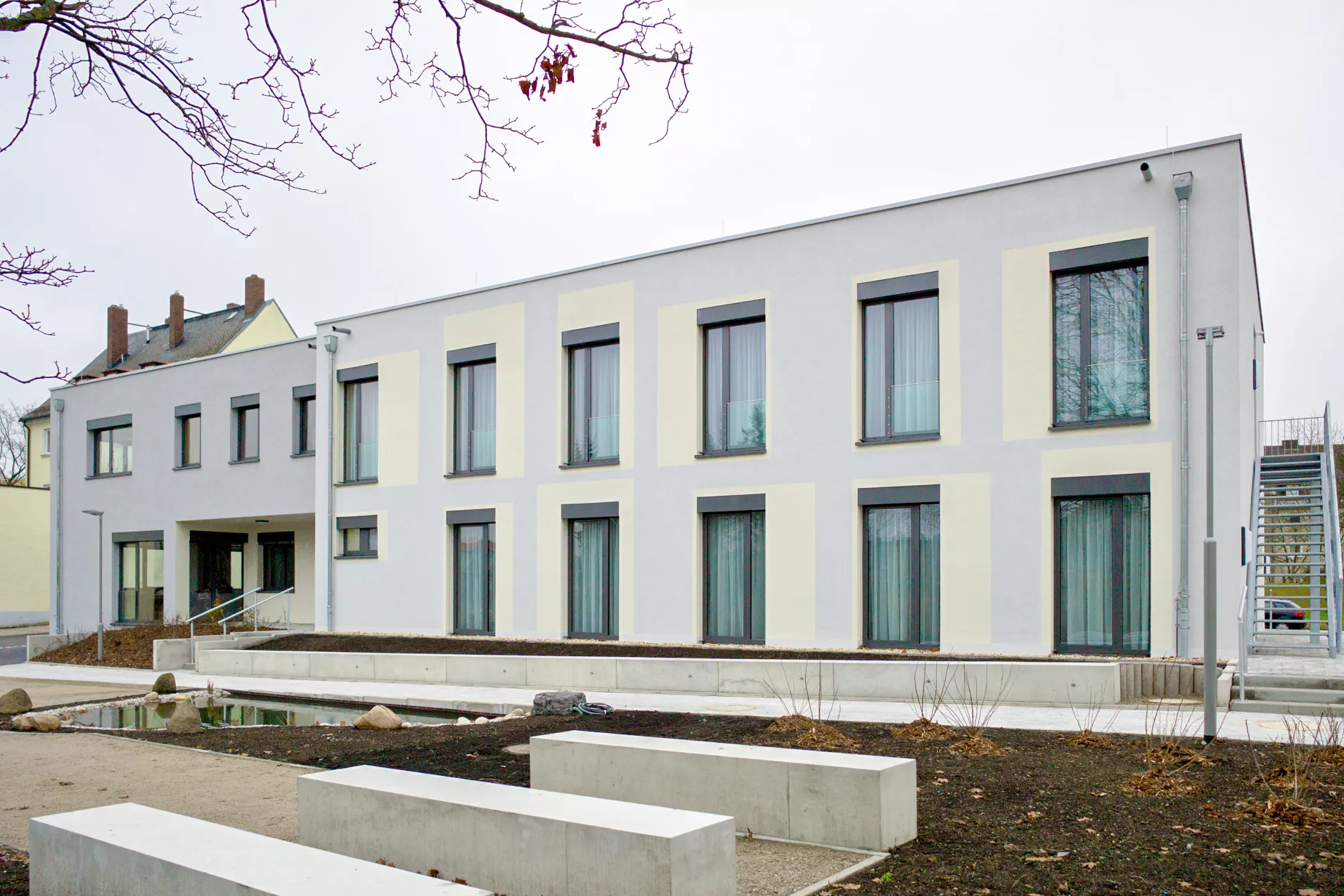 2-stöckiges weißes Gebäude mit bodentiefen Fenstern.