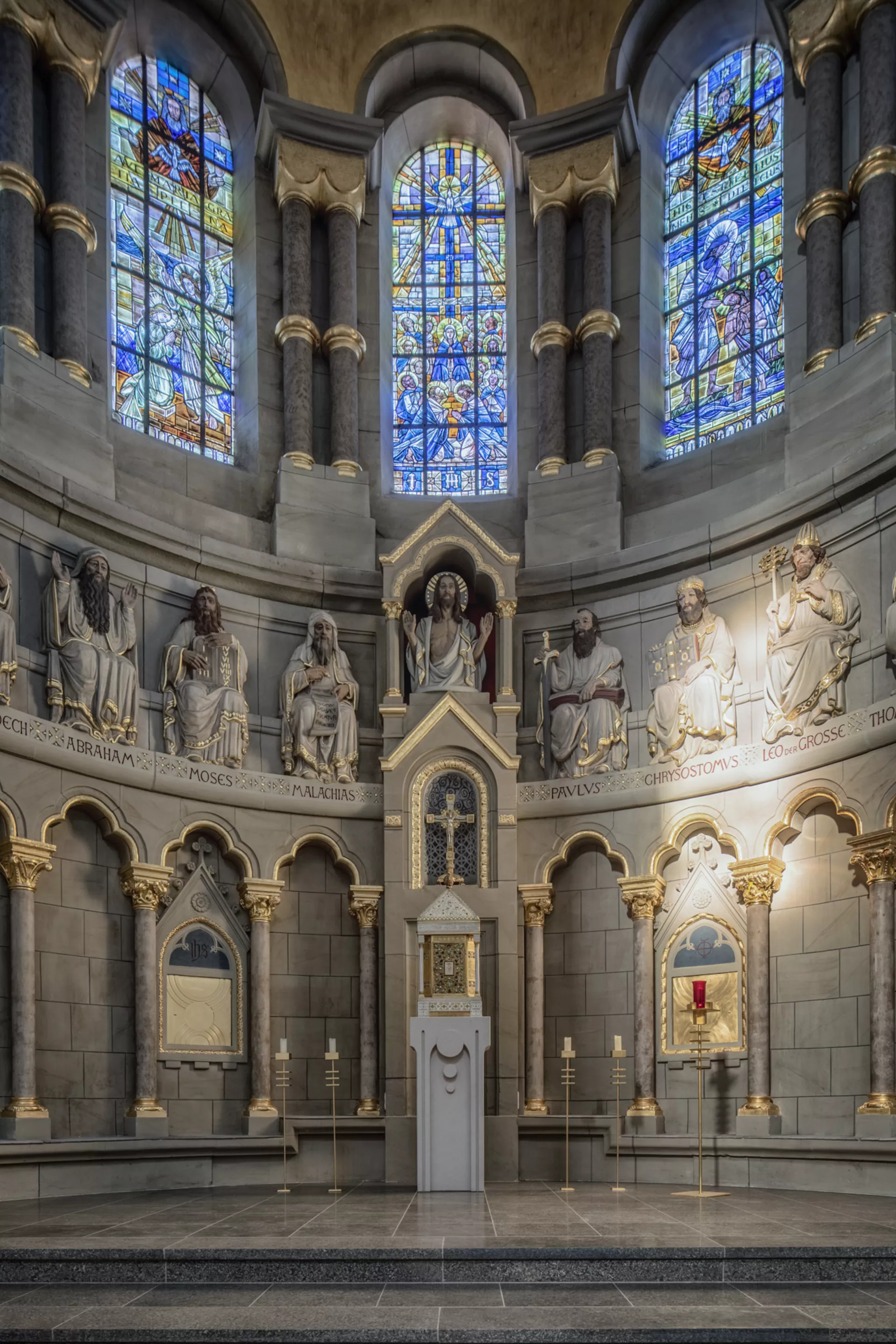 Ein halbkreisförmiger Altarbereich einer Kirche, die Wand ist gesäumt von kleinen Säulen und den Statuen bedeutender Personen der christlichen Religionsgeschichte.