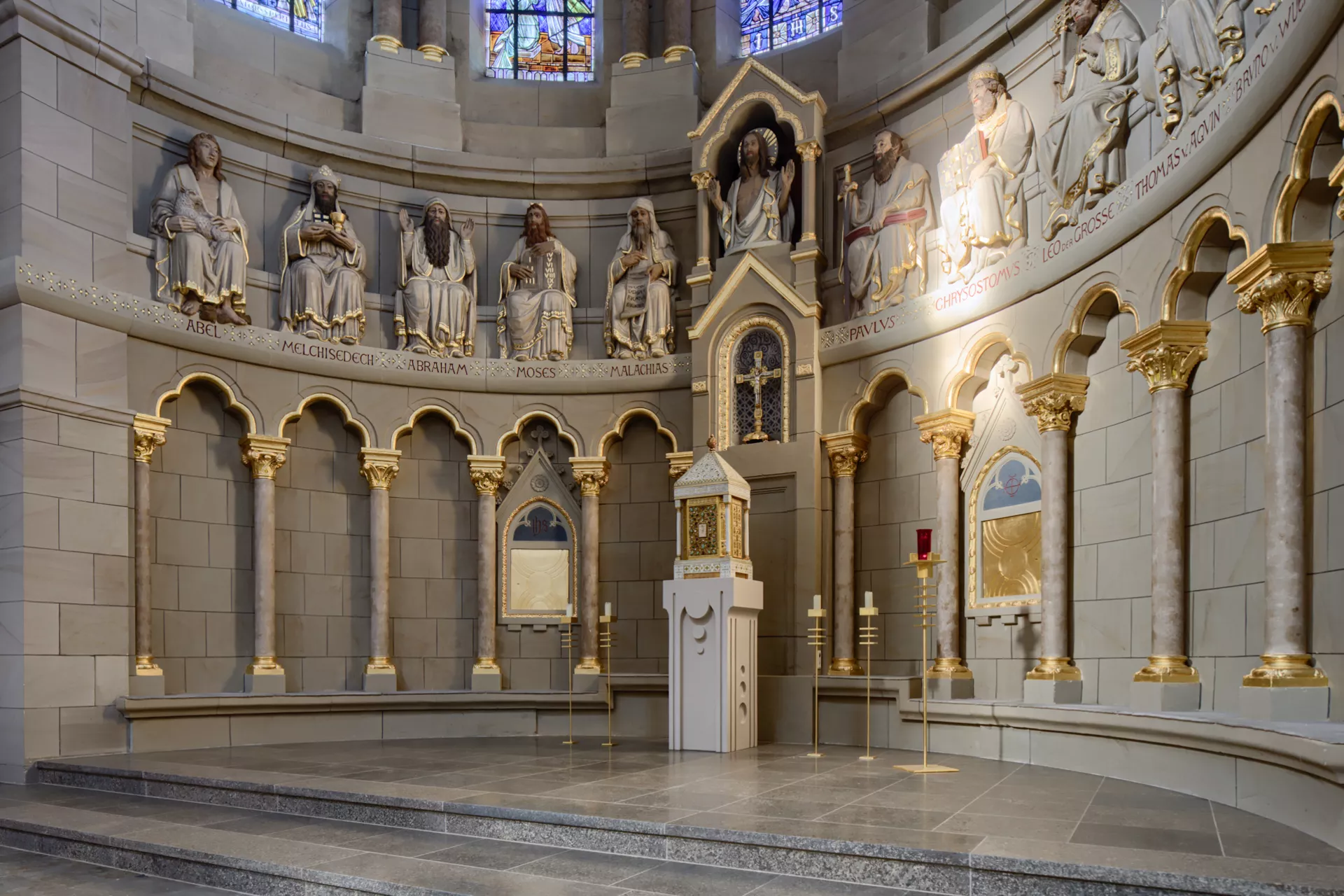 Ein halbkreisförmiger Altarbereich einer Kirche, die Wand ist gesäumt von kleinen Säulen und den Statuen bedeutender Personen der christlichen Religionsgeschichte.