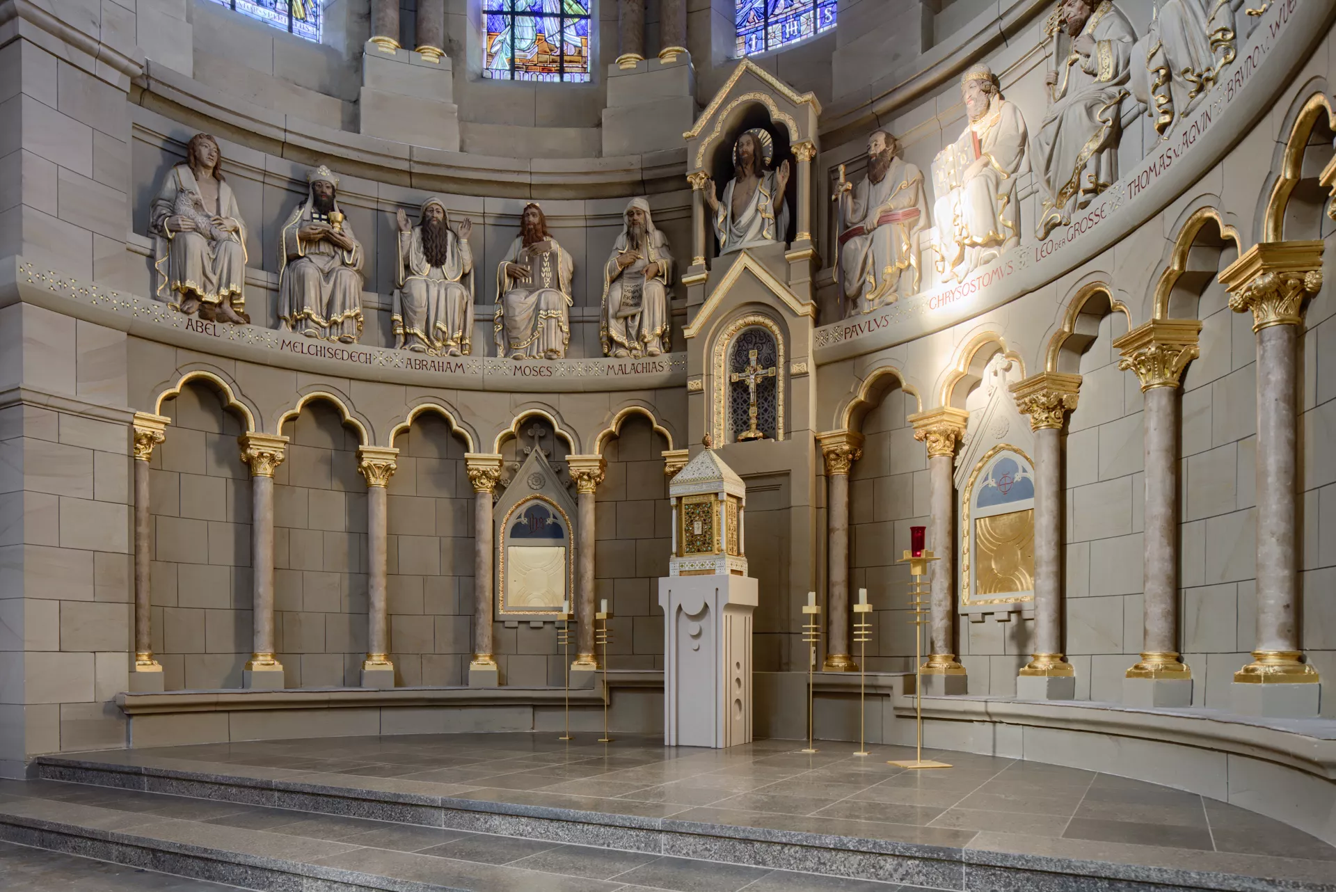 Ein halbkreisförmiger Altarbereich einer Kirche, die Wand ist gesäumt von kleinen Säulen und den Statuen bedeutender Personen der christlichen Religionsgeschichte.